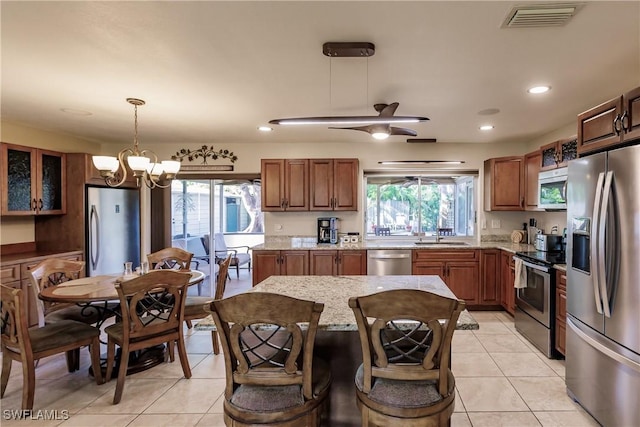 kitchen featuring light stone counters, light tile patterned floors, pendant lighting, plenty of natural light, and appliances with stainless steel finishes