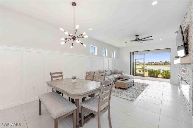 dining space featuring a fireplace, light tile patterned floors, and ceiling fan with notable chandelier