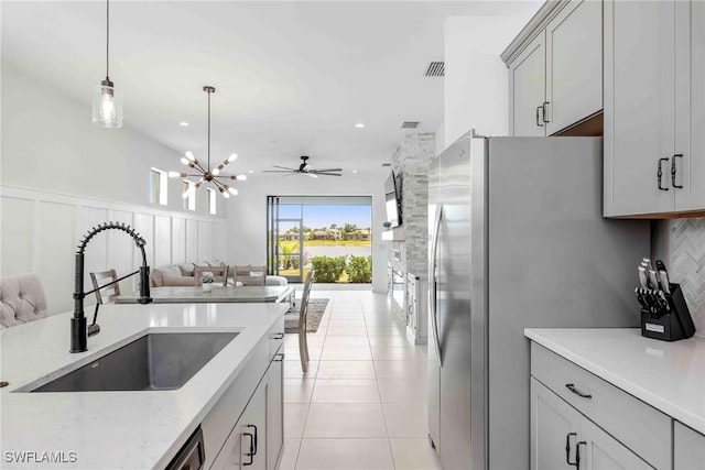 kitchen with gray cabinetry, sink, pendant lighting, decorative backsplash, and ceiling fan with notable chandelier