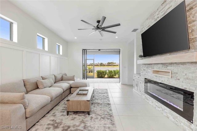 living room with light tile patterned floors, a stone fireplace, ceiling fan, and a healthy amount of sunlight