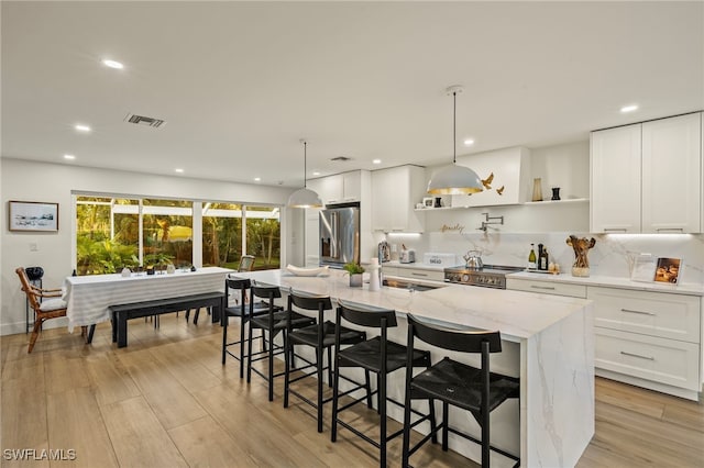 kitchen featuring light stone counters, stainless steel appliances, decorative light fixtures, a center island with sink, and white cabinets