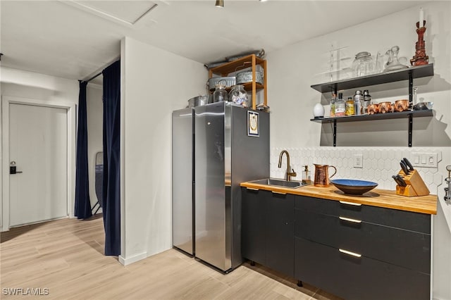 kitchen with wood counters, light wood-type flooring, sink, and stainless steel refrigerator