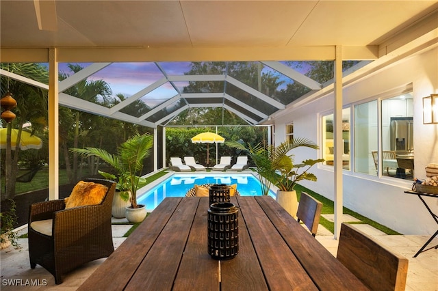 pool at dusk with glass enclosure and a patio