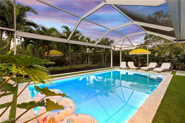 pool at dusk featuring glass enclosure and a patio area