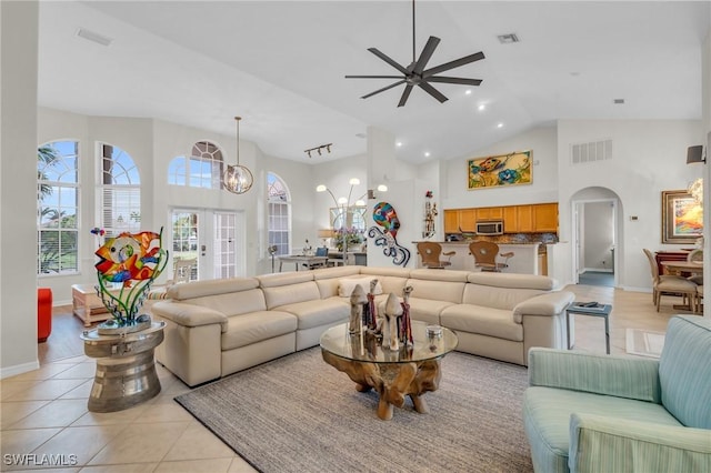 tiled living room with french doors, ceiling fan with notable chandelier, and high vaulted ceiling