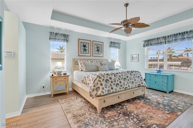 bedroom with multiple windows, light hardwood / wood-style flooring, a raised ceiling, and ceiling fan