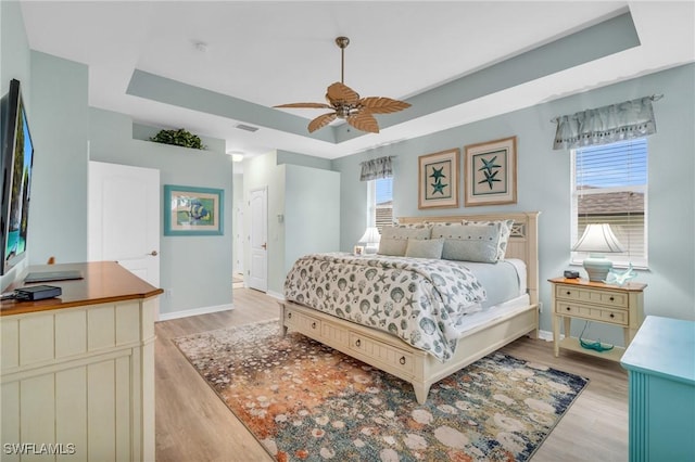 bedroom with a raised ceiling, ceiling fan, and light hardwood / wood-style flooring