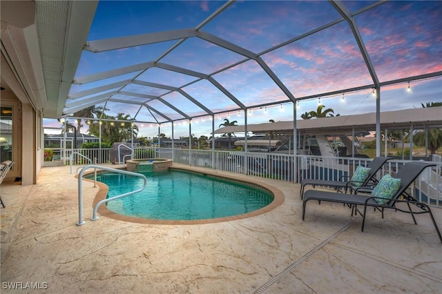 pool at dusk with a lanai, an in ground hot tub, and a patio