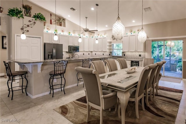 dining area featuring wine cooler, light tile patterned flooring, ceiling fan with notable chandelier, and high vaulted ceiling