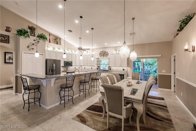 tiled dining room with high vaulted ceiling, a healthy amount of sunlight, and ceiling fan with notable chandelier