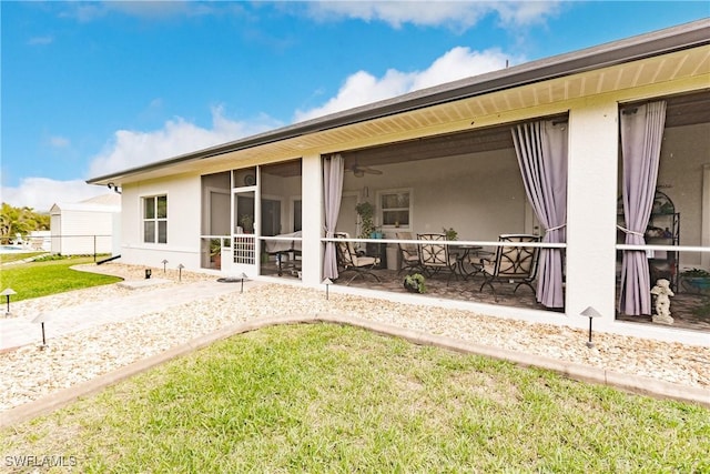 back of property with a lawn, a sunroom, and ceiling fan