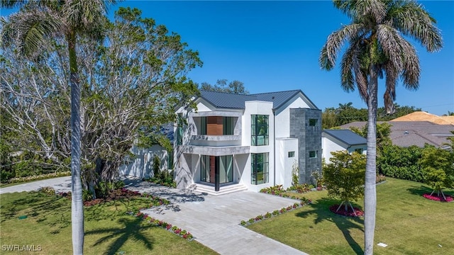 view of front of house featuring stucco siding, metal roof, a front lawn, a balcony, and a standing seam roof
