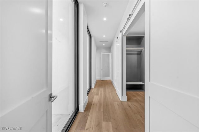 corridor featuring baseboards, a barn door, light wood-style flooring, and recessed lighting
