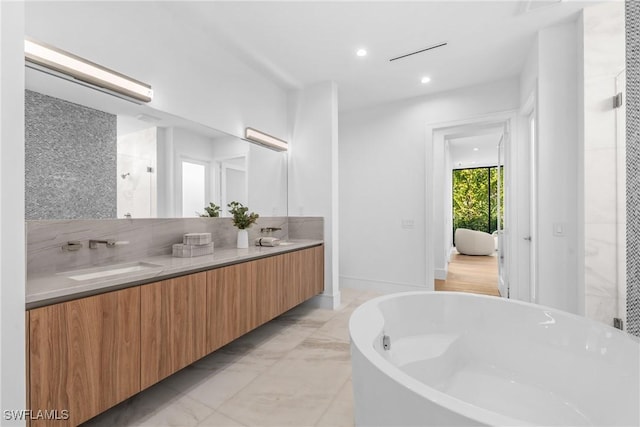 full bath with double vanity, a sink, a freestanding bath, marble finish floor, and recessed lighting