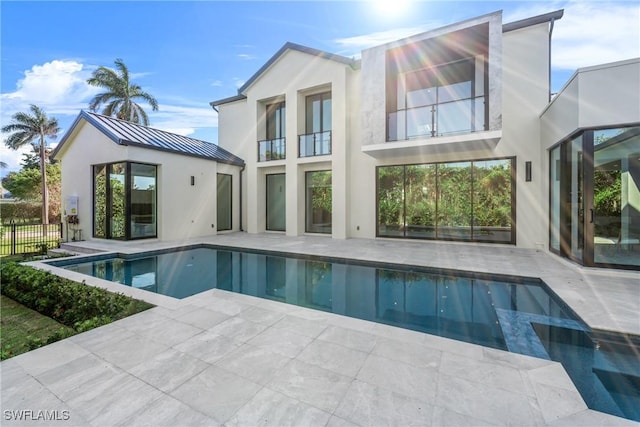 back of house featuring a patio area, a standing seam roof, metal roof, and a fenced in pool