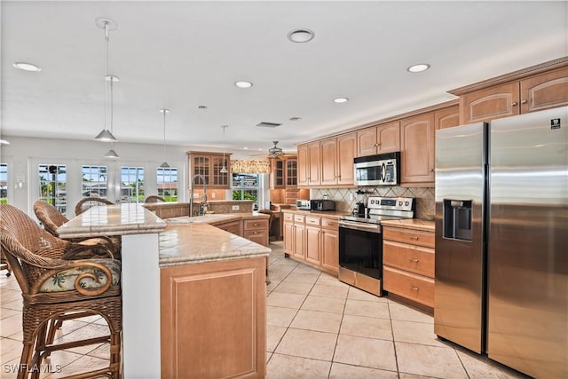 kitchen with sink, stainless steel appliances, an island with sink, decorative light fixtures, and light tile patterned floors