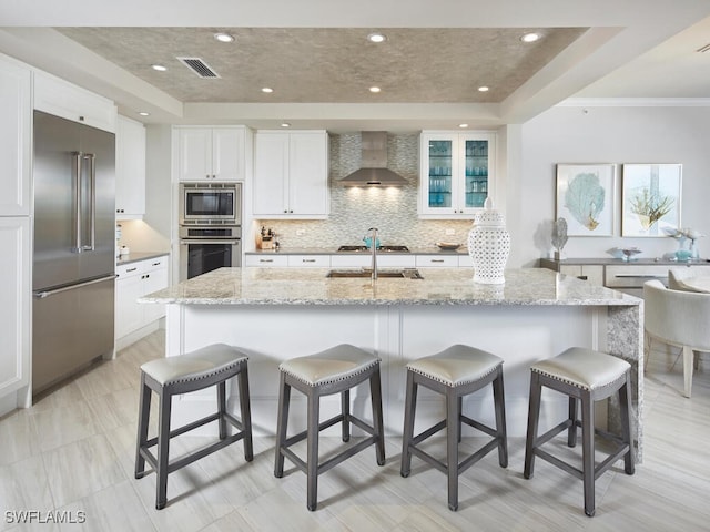 kitchen featuring a kitchen breakfast bar, white cabinetry, wall chimney exhaust hood, and appliances with stainless steel finishes