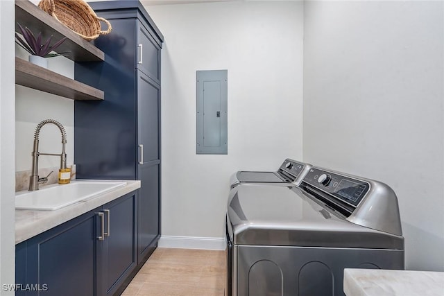 clothes washing area featuring cabinets, sink, light hardwood / wood-style flooring, washing machine and clothes dryer, and electric panel