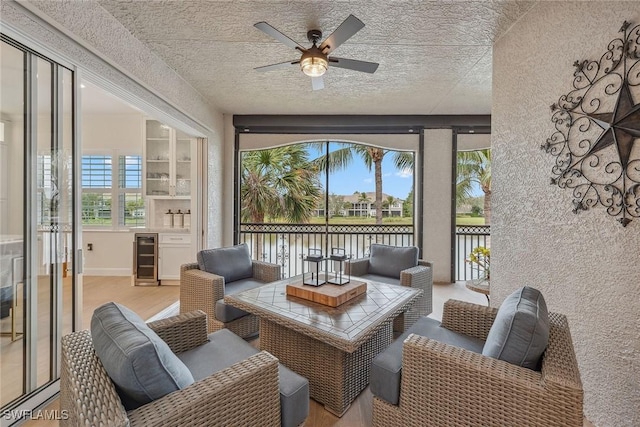 sunroom featuring ceiling fan, a water view, and beverage cooler