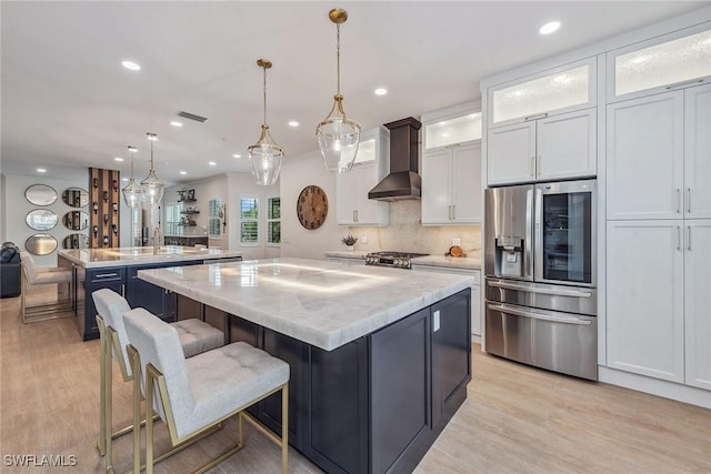 kitchen featuring a center island, pendant lighting, wall chimney range hood, and stainless steel refrigerator with ice dispenser