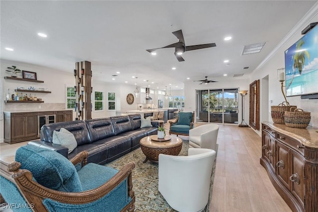 living room featuring ceiling fan, light wood-type flooring, crown molding, and bar