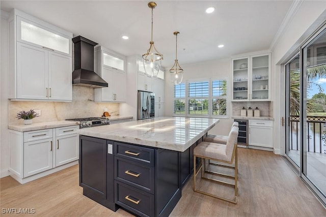 kitchen featuring white cabinets, wall chimney exhaust hood, a kitchen island, stainless steel appliances, and beverage cooler