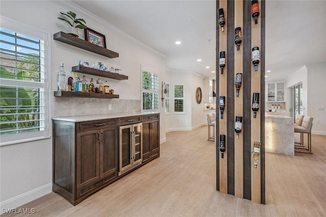 bar with backsplash, dark brown cabinets, light hardwood / wood-style floors, and crown molding