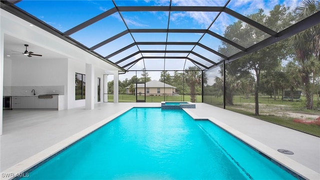 view of pool featuring glass enclosure, an outdoor kitchen, sink, a patio, and ceiling fan