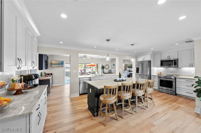 kitchen with white cabinets, a center island, decorative light fixtures, stainless steel appliances, and backsplash