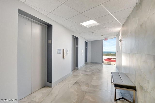 hall with a paneled ceiling, elevator, and expansive windows