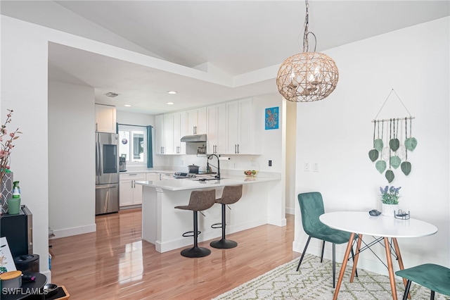 kitchen featuring kitchen peninsula, stainless steel fridge, vaulted ceiling, sink, and white cabinetry