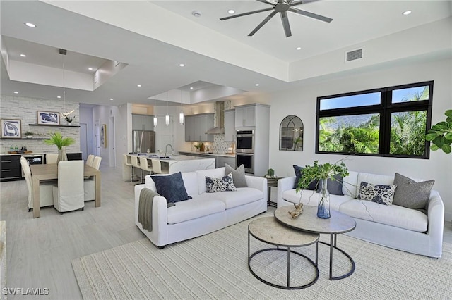 living room with ceiling fan and a tray ceiling