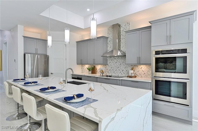 kitchen with backsplash, wall chimney range hood, sink, a kitchen island with sink, and appliances with stainless steel finishes