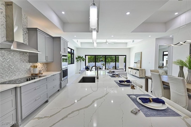 kitchen featuring tasteful backsplash, black electric stovetop, sink, gray cabinetry, and wall chimney exhaust hood