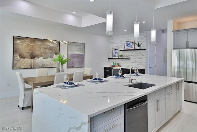 kitchen with gray cabinets, sink, light stone countertops, an island with sink, and stainless steel appliances