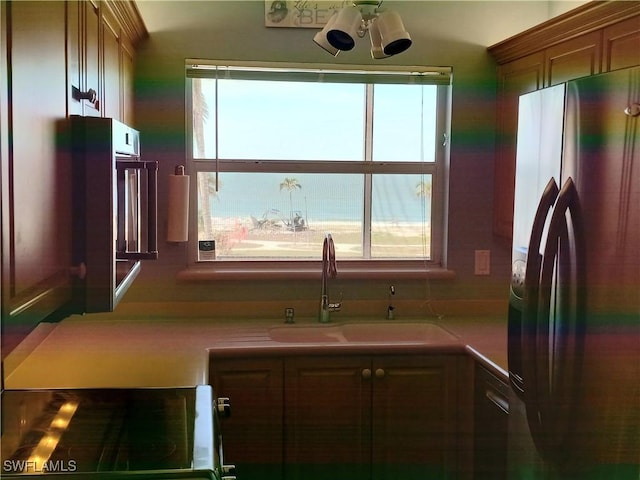 kitchen with a healthy amount of sunlight, sink, stainless steel refrigerator, and stove