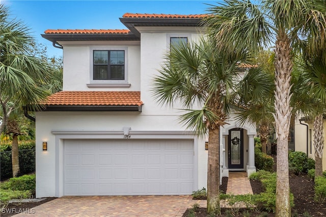 mediterranean / spanish house featuring stucco siding, a tile roof, decorative driveway, and a garage