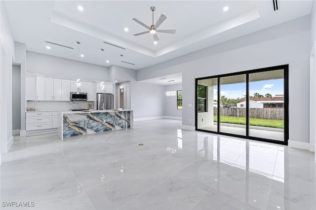 unfurnished living room featuring ceiling fan, a raised ceiling, and a towering ceiling