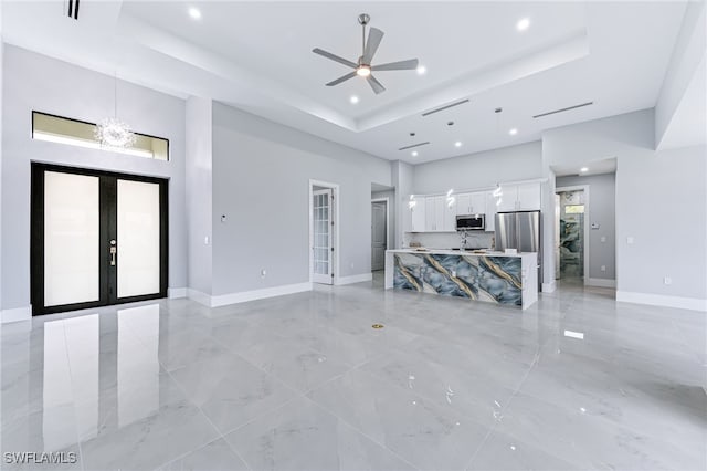 unfurnished living room with ceiling fan with notable chandelier, a towering ceiling, a tray ceiling, and french doors