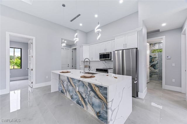 kitchen featuring appliances with stainless steel finishes, light stone counters, a kitchen island with sink, decorative light fixtures, and white cabinetry