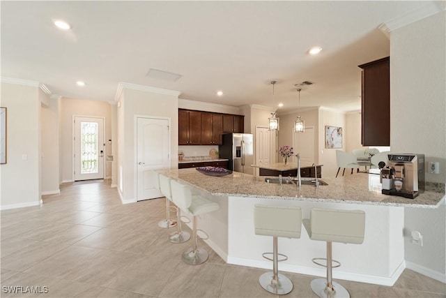 kitchen with pendant lighting, sink, light stone counters, ornamental molding, and stainless steel fridge with ice dispenser