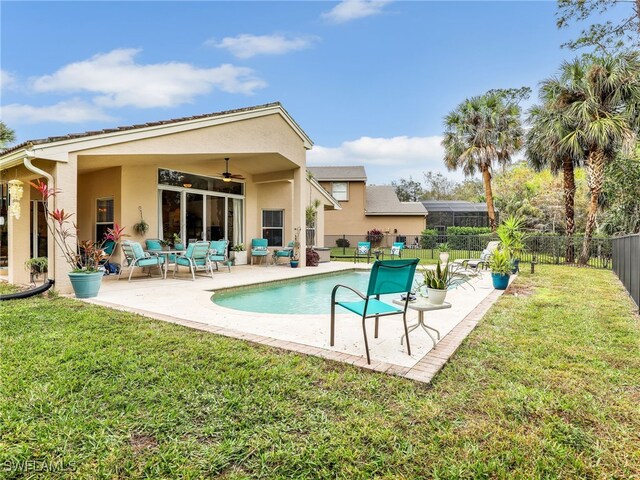rear view of house with stucco siding, fence, ceiling fan, and a lawn