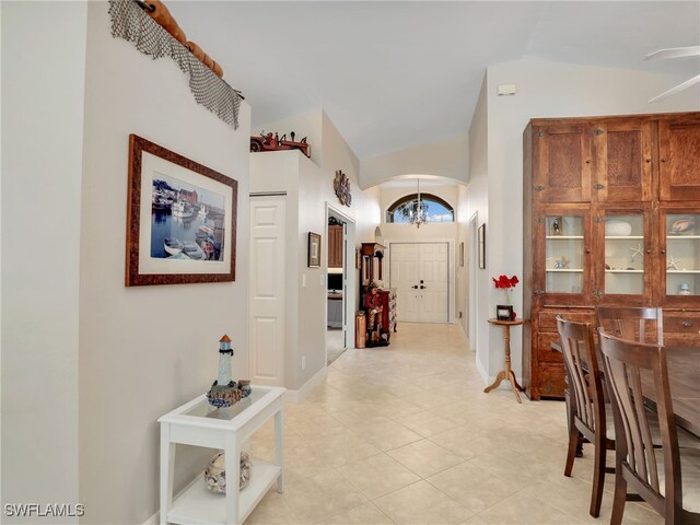 hallway featuring vaulted ceiling, light tile patterned floors, arched walkways, baseboards, and a chandelier