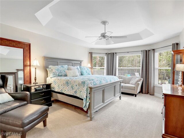 bedroom with a tray ceiling, multiple windows, a ceiling fan, and light carpet