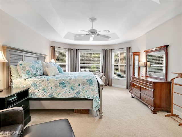 bedroom featuring ceiling fan, a tray ceiling, and light carpet