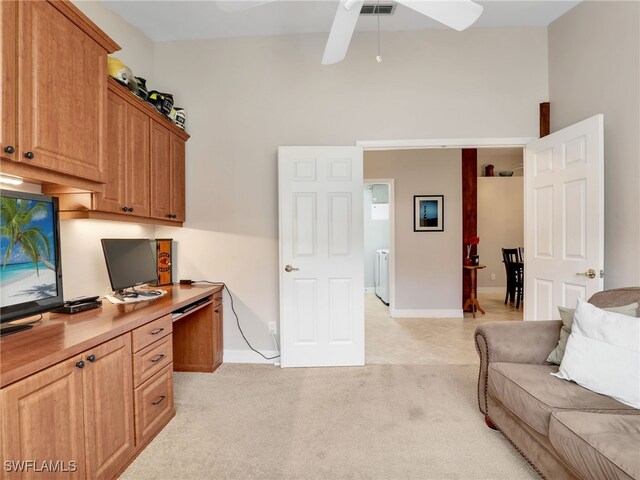 office space featuring built in desk, ceiling fan, washer / dryer, light colored carpet, and baseboards