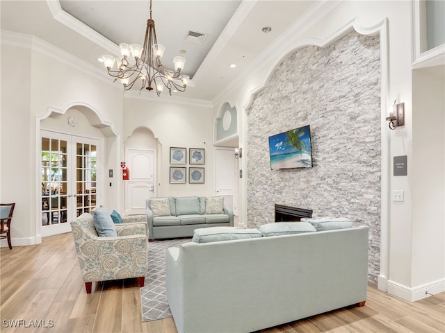 living room with a fireplace, french doors, a tray ceiling, crown molding, and light hardwood / wood-style flooring