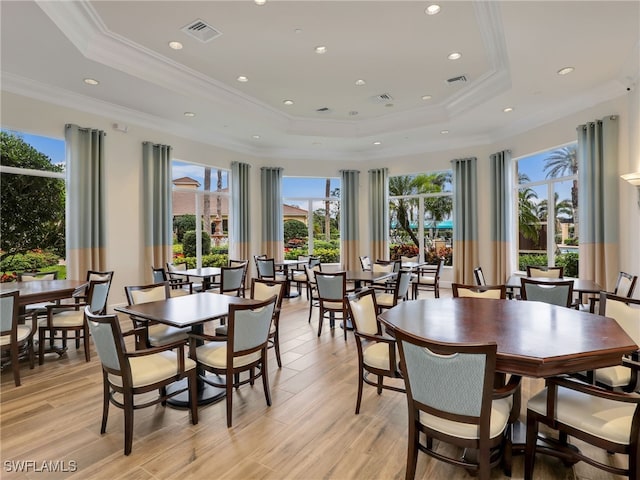 dining space featuring a tray ceiling, ornamental molding, and light wood-type flooring