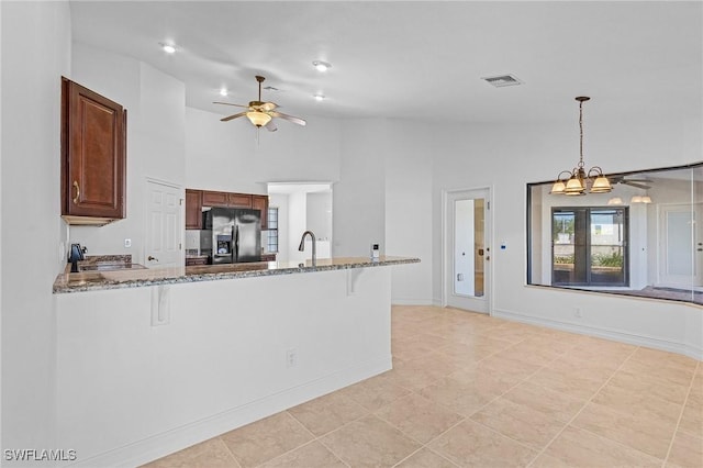 kitchen featuring stainless steel fridge with ice dispenser, kitchen peninsula, decorative light fixtures, a kitchen breakfast bar, and light stone countertops