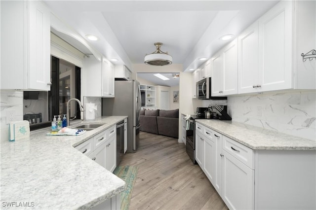 kitchen featuring light stone countertops, appliances with stainless steel finishes, decorative backsplash, white cabinets, and light wood-type flooring